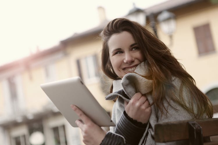 Smiling Woman Messaging On Tablet In City