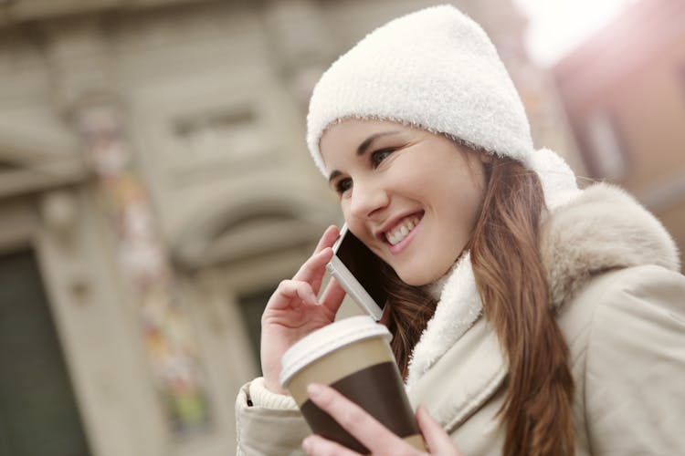 Charming Woman With Takeaway Coffee Speaking On Smartphone In City