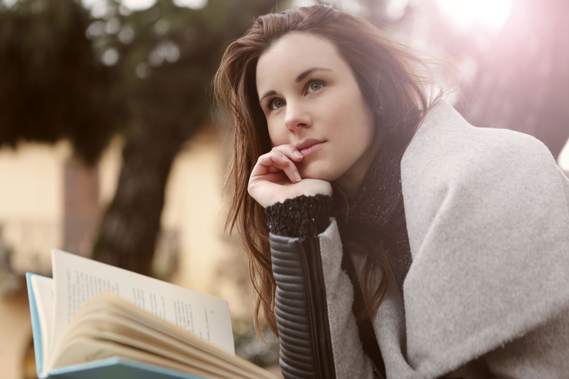 A young woman in deep thought while reading outdoors, captured in warm daylight.