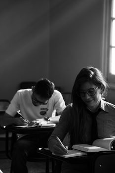 Students engaged in study in a dimly lit classroom, captured in black and white.
