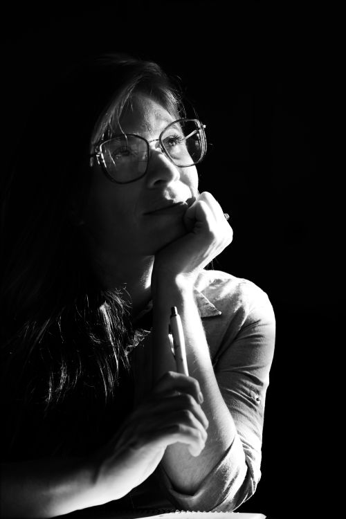 Free Black and white portrait of a thoughtful woman with glasses, holding a pen, in a contemplative pose. Stock Photo