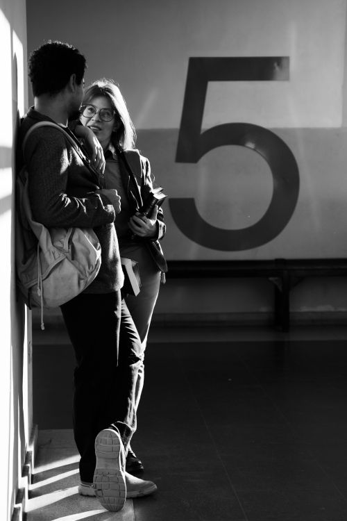 Free Black and white photo of two students talking near a large number 5 indoors. Stock Photo