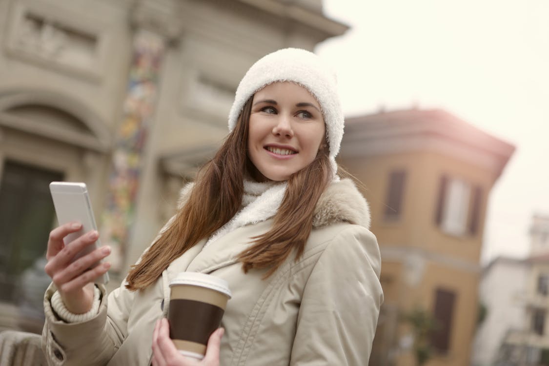Woman in White Knit Cap Holding Brown and White Disposable Cup