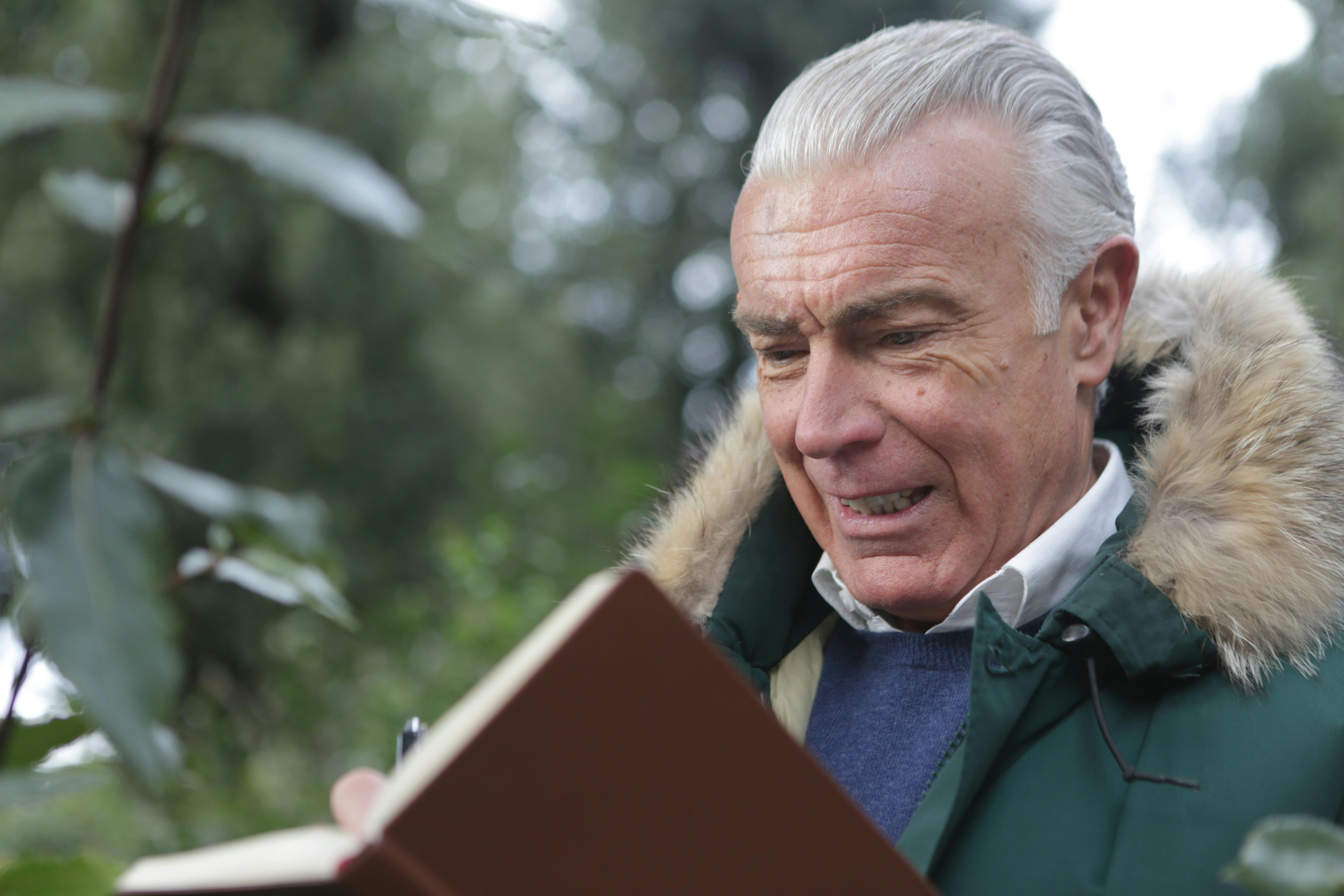 sad elderly man writing on brown notebook