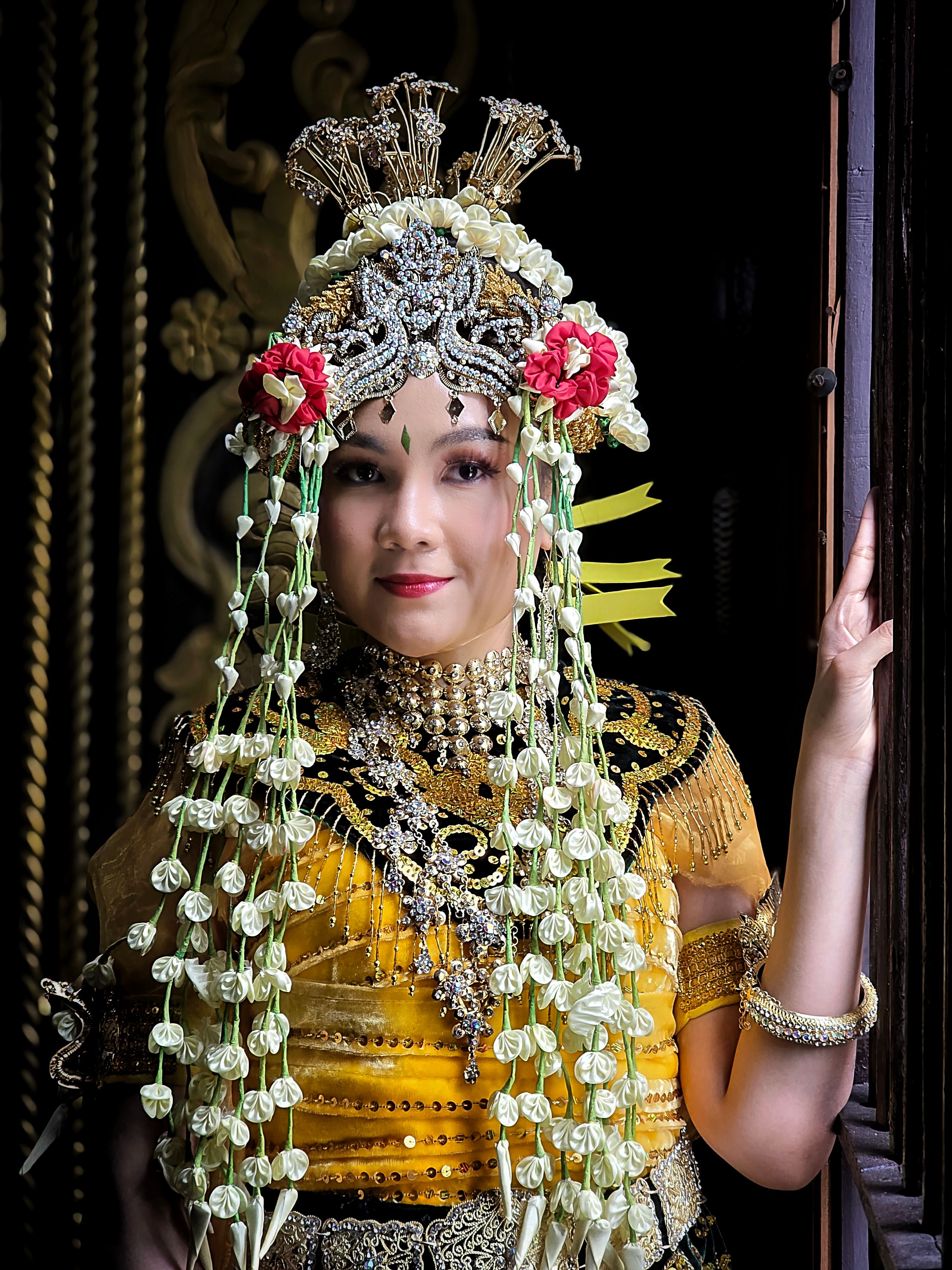 Portrait of a woman in traditional Indonesian wedding attire with intricate gold and floral decorations.