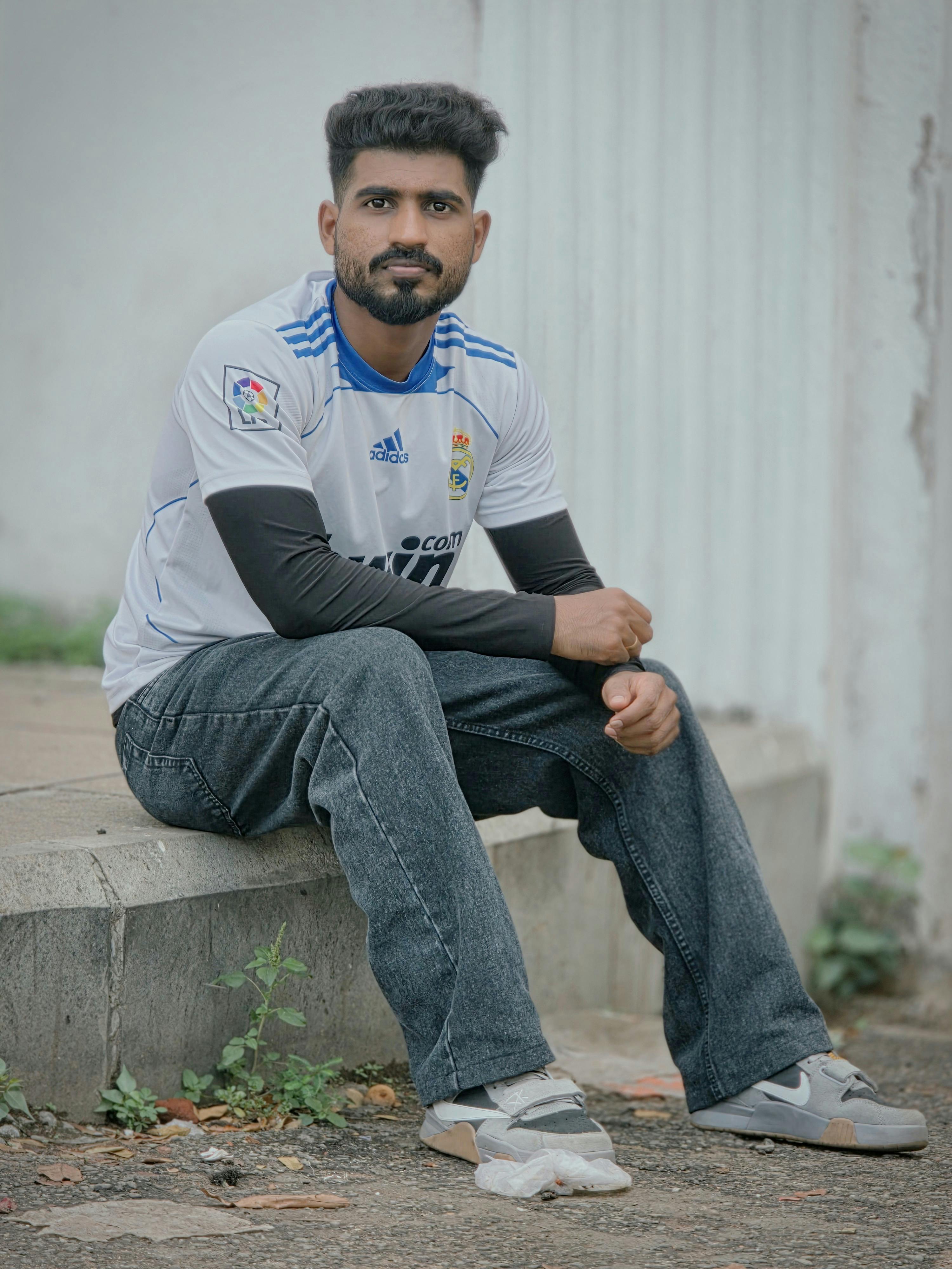 A man in casual sportswear sits outdoors on a concrete ledge, exuding a relaxed vibe.
