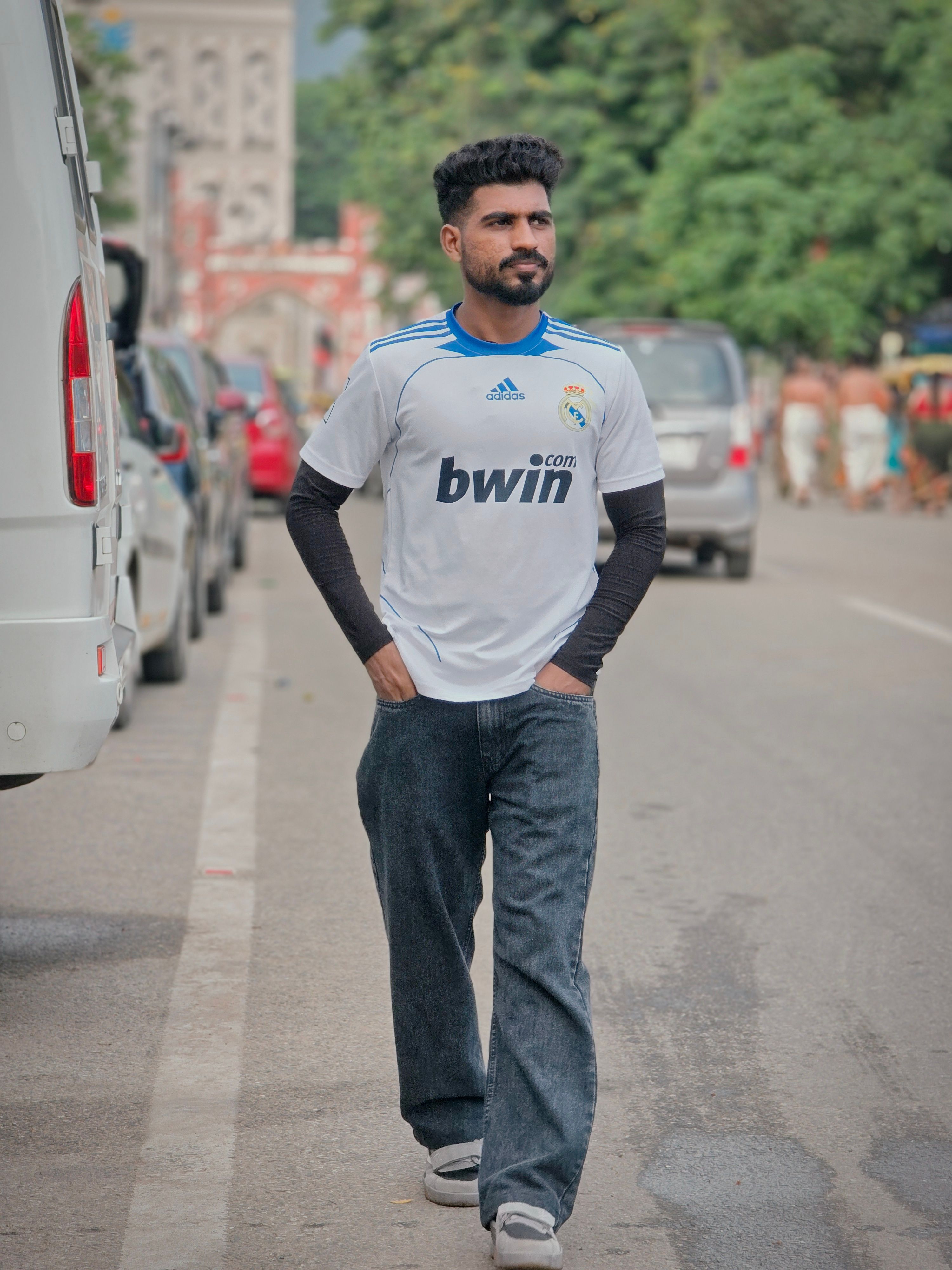 Man strolling on a busy city street lined with vehicles and trees.