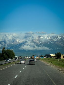 Cars driving on a highway with a stunning view of snow-capped mountains and clear blue sky.