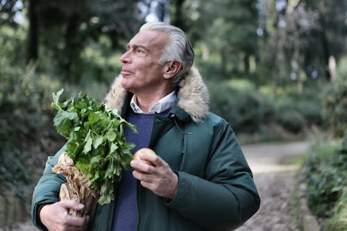 Man in Green Jacket Holding Brown Paper Bag with Green Leaves