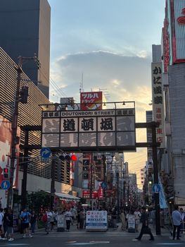Explore the vibrant atmosphere of Dotonbori Street in Osaka at sunset, with bustling crowds and vivid signage.