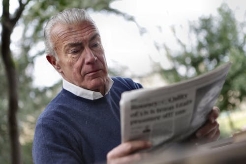 Man in Blue Sweater Reading Newspapers