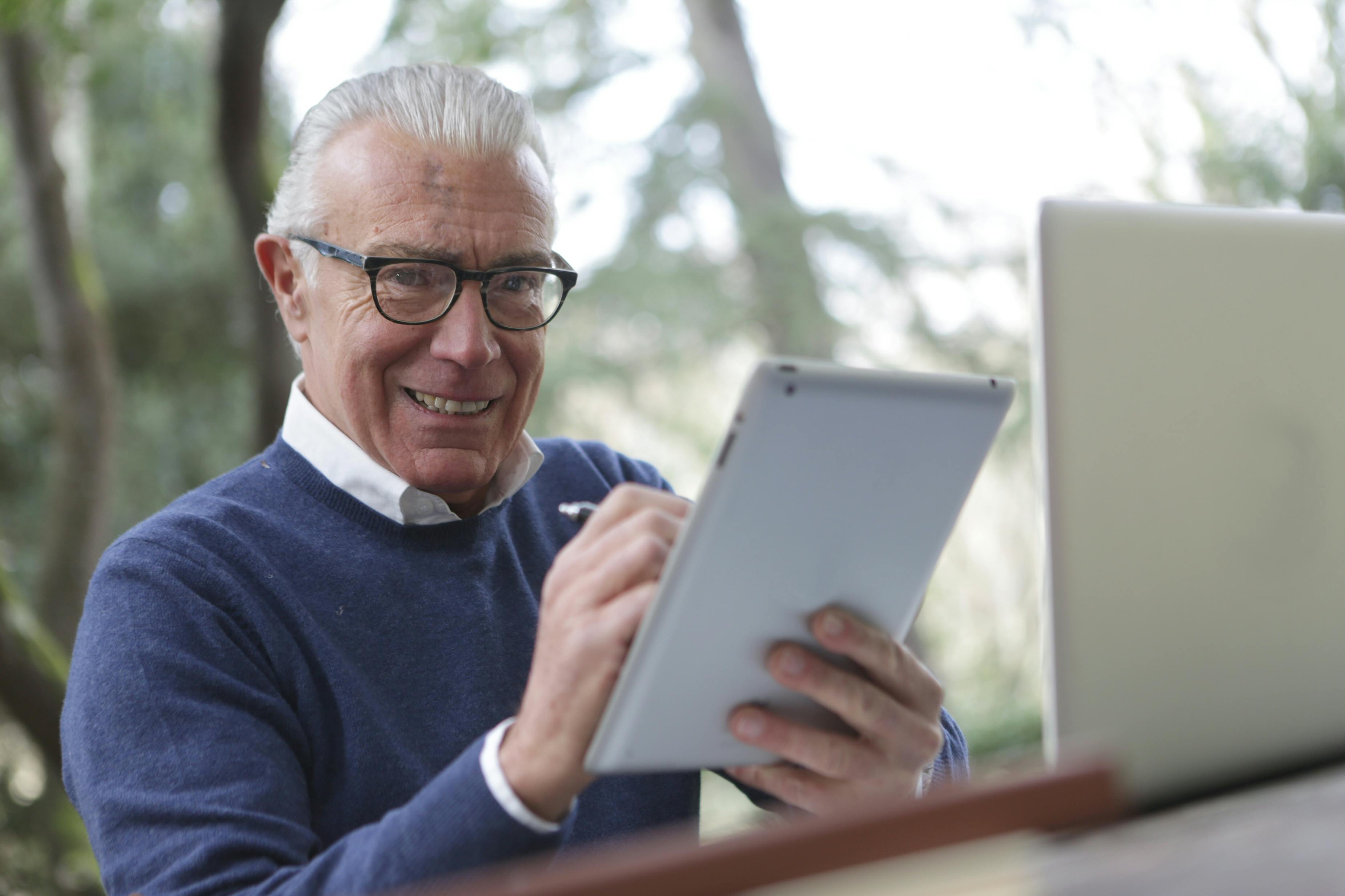 man in blue sweater holding white tablet computer