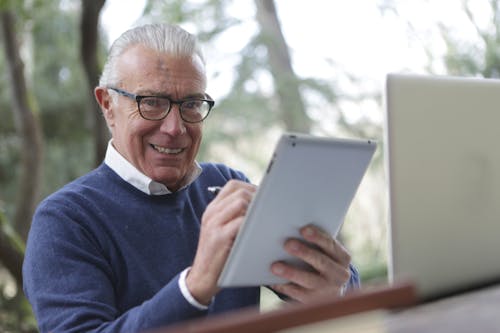Man in Blue Sweater Holding White Tablet Computer