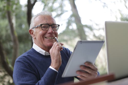 Man in Blue Sweater Holding White Tablet Computer