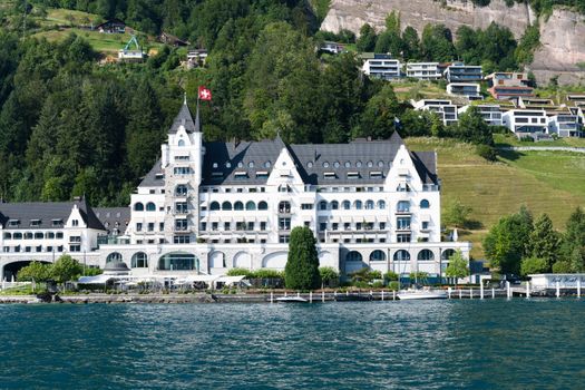 Stunning Swiss hotel by the lakeside with lush mountains and a clear blue sky.