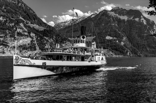Free Black and white photo of a classic steamboat cruising on a lake with majestic mountains in the background. Stock Photo