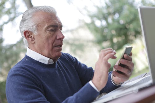 Man in Blue Sweater Holding Smartphone Using Remote Care App