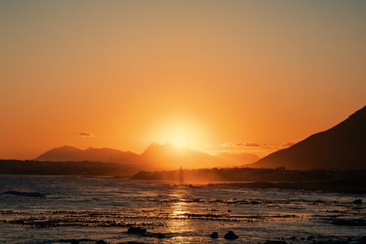 Stunning sunset over the ocean with mountains in the background, creating a warm and serene atmosphere.