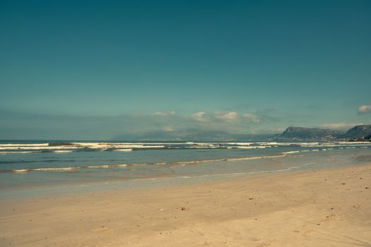 Peaceful beach scene capturing gentle waves and distant mountains under a clear sky.