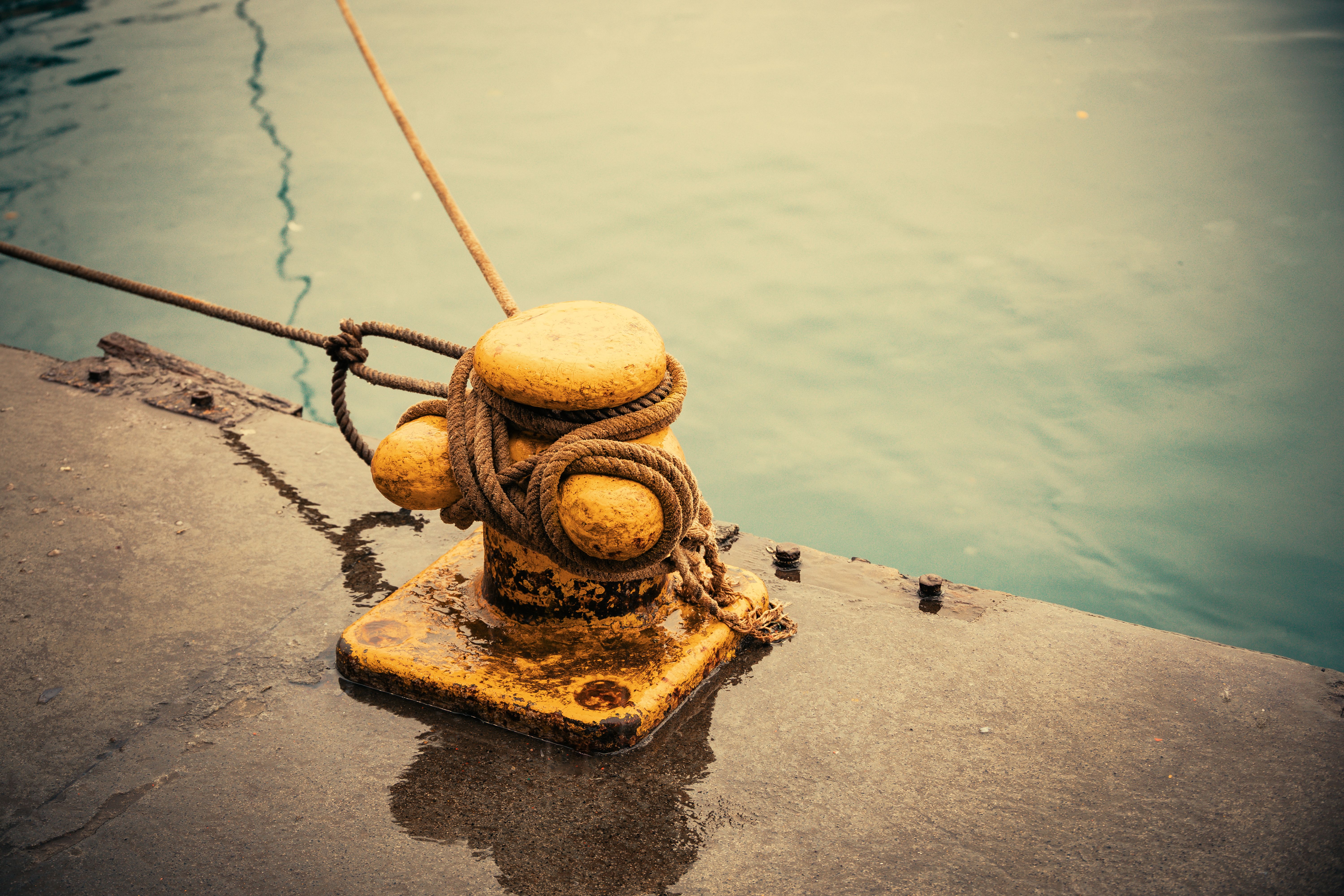 Weathered bollard with ropes on a pier over calm water. Captures nautical theme.
