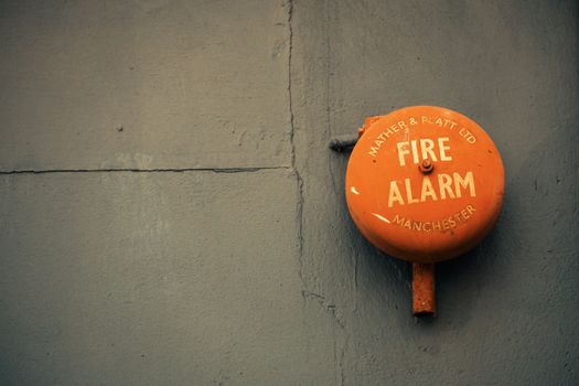 Close-up of an old fire alarm on a gray concrete wall, with text 'Mather & Platt Ltd Fire Alarm Manchester.'