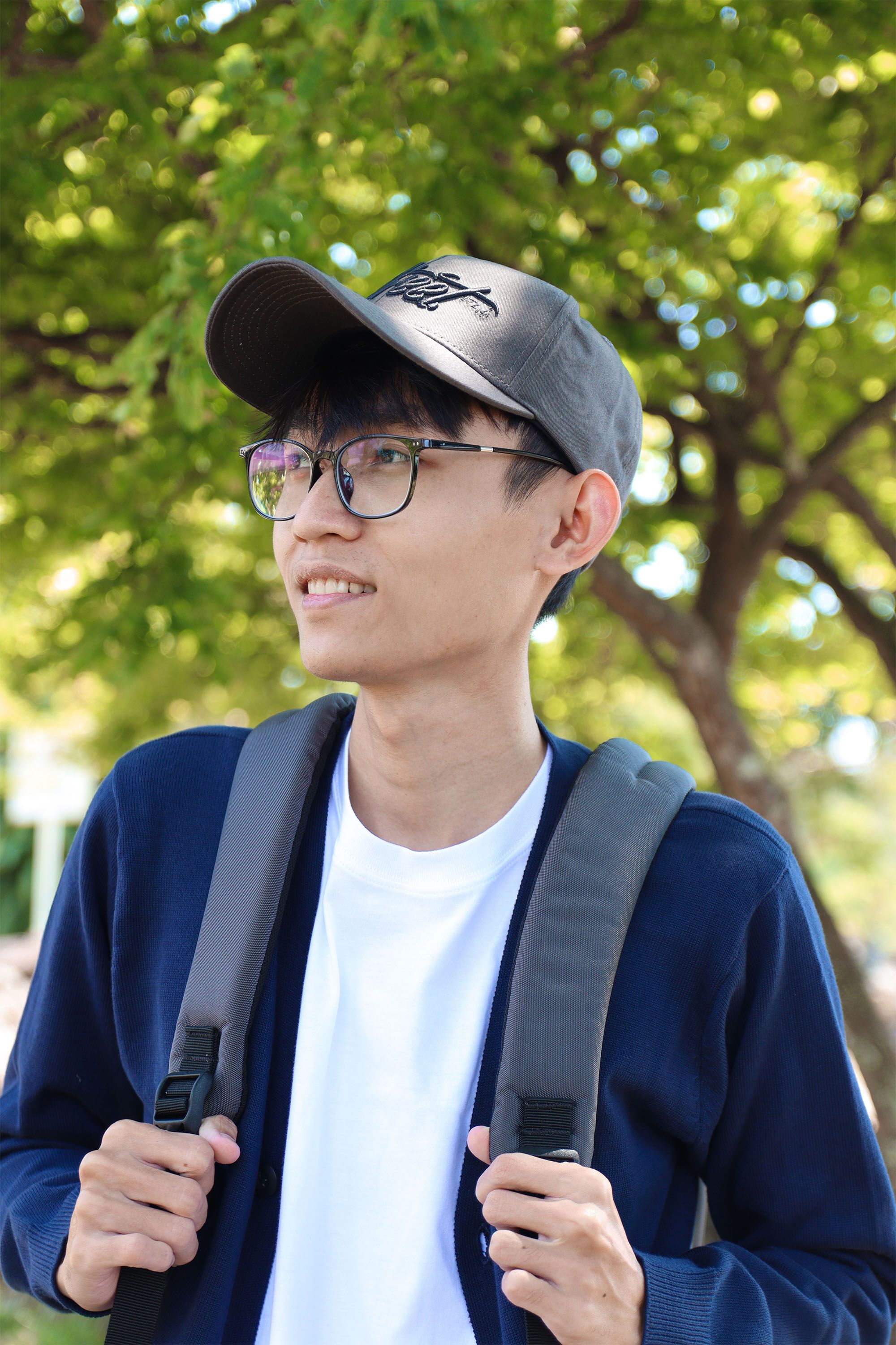 Smiling young man with backpack outdoors in a sunny park.