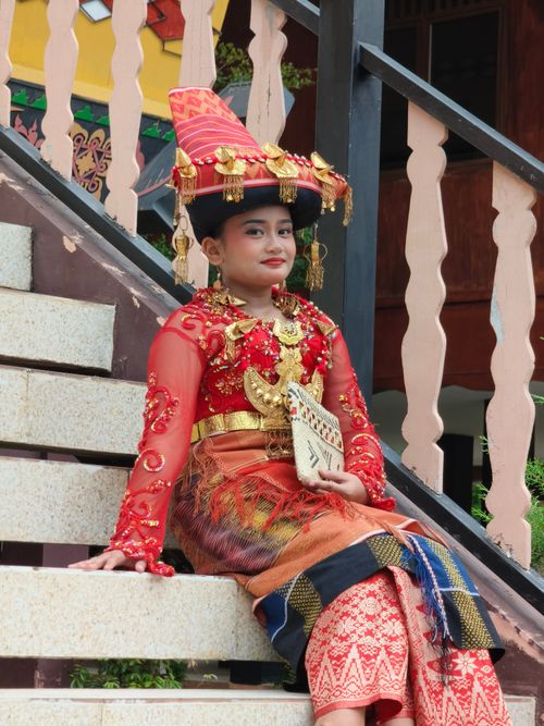 Free A young girl in vibrant Indonesian traditional attire seated on a staircase in Jakarta. Stock Photo