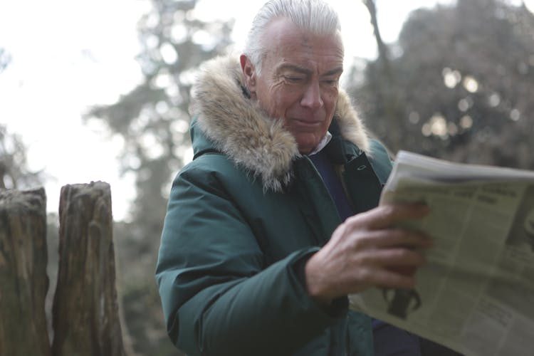 Man In Green Parka Jacket Reading News Paper