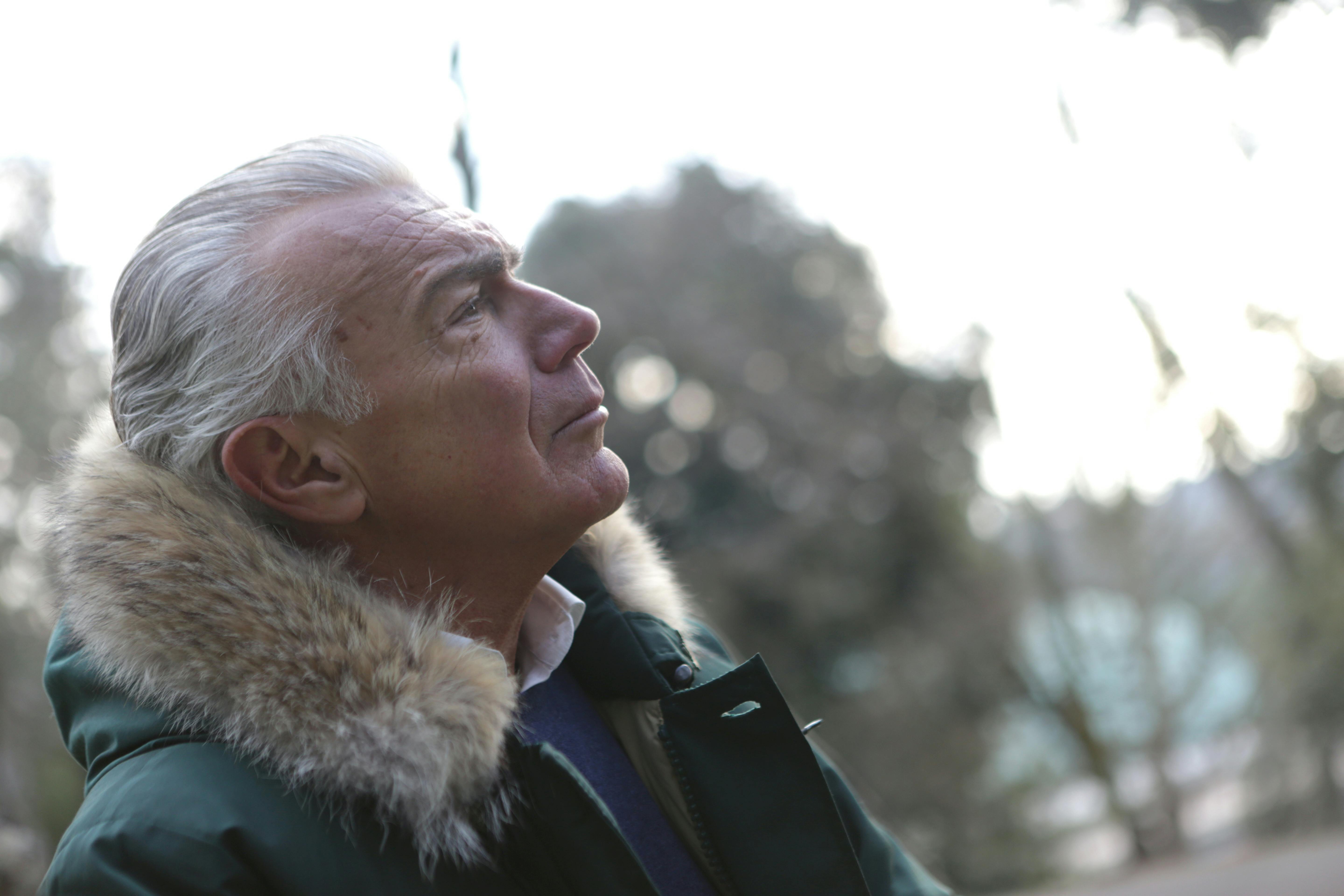 man in green parka jacket looking up the sky