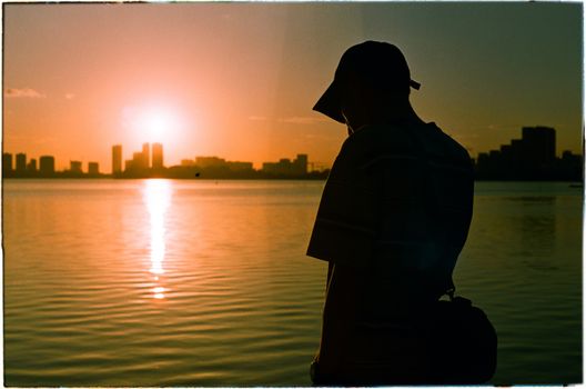 Silhouette of a person at sunset by a city waterfront, creating a serene ambiance.