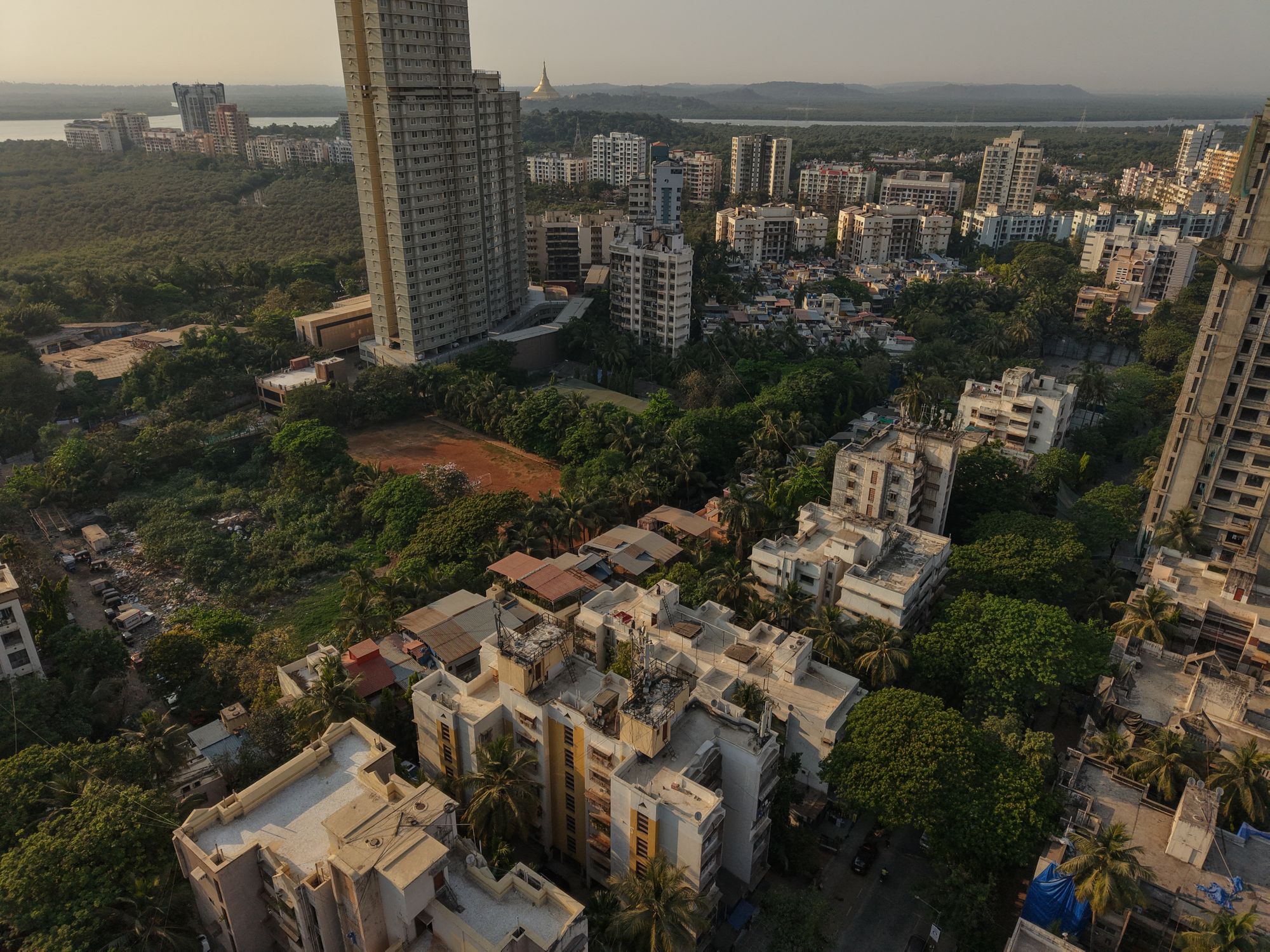 Aerial shot of dense residential skyscrapers in Mumbai, surrounded by green areas at dusk.