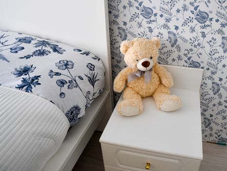 A cozy children's room in Finland featuring floral bedding and a cute teddy bear on a white nightstand.