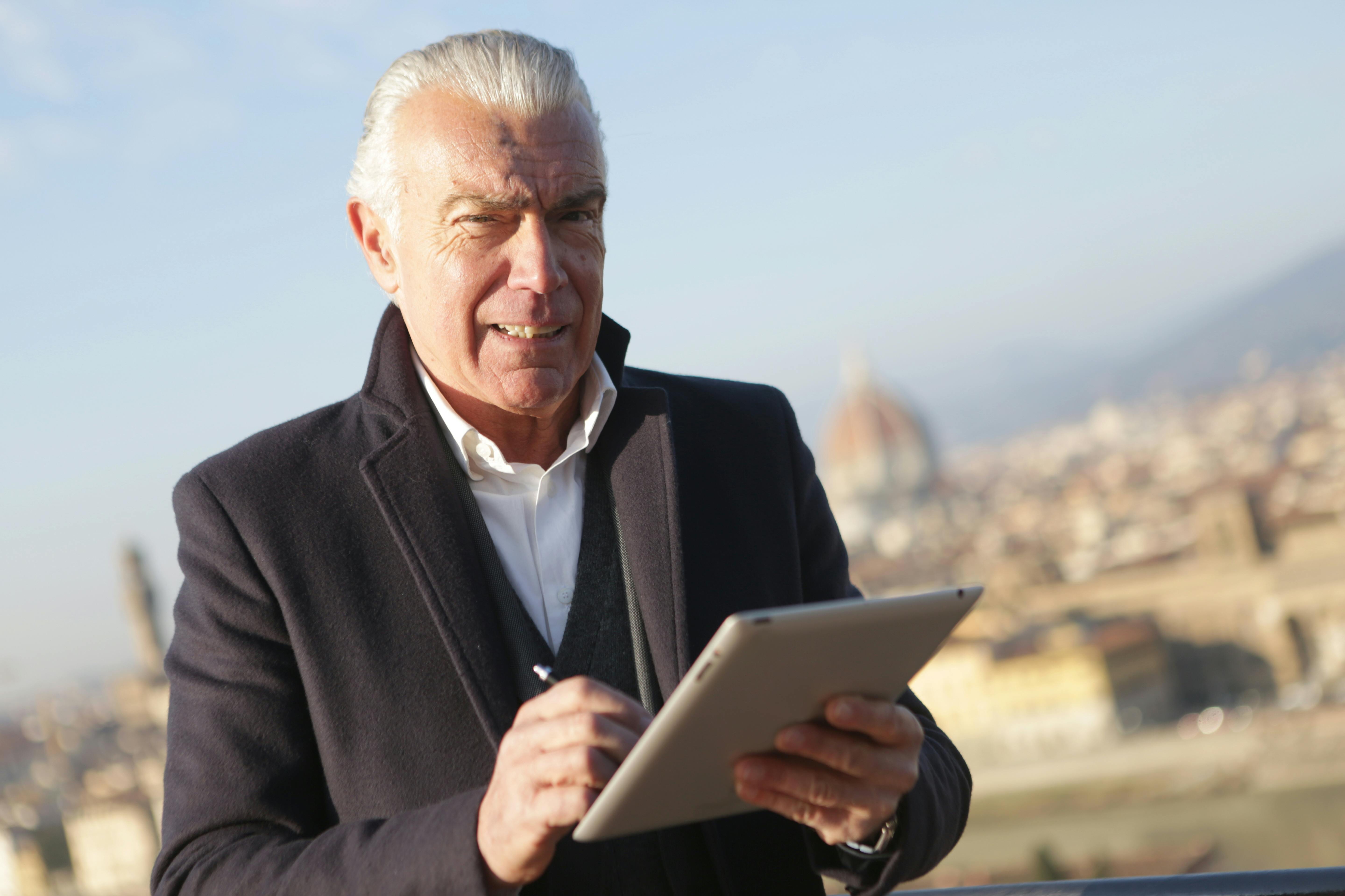 man in black suit jacket holding silver ipad and black stylus pen