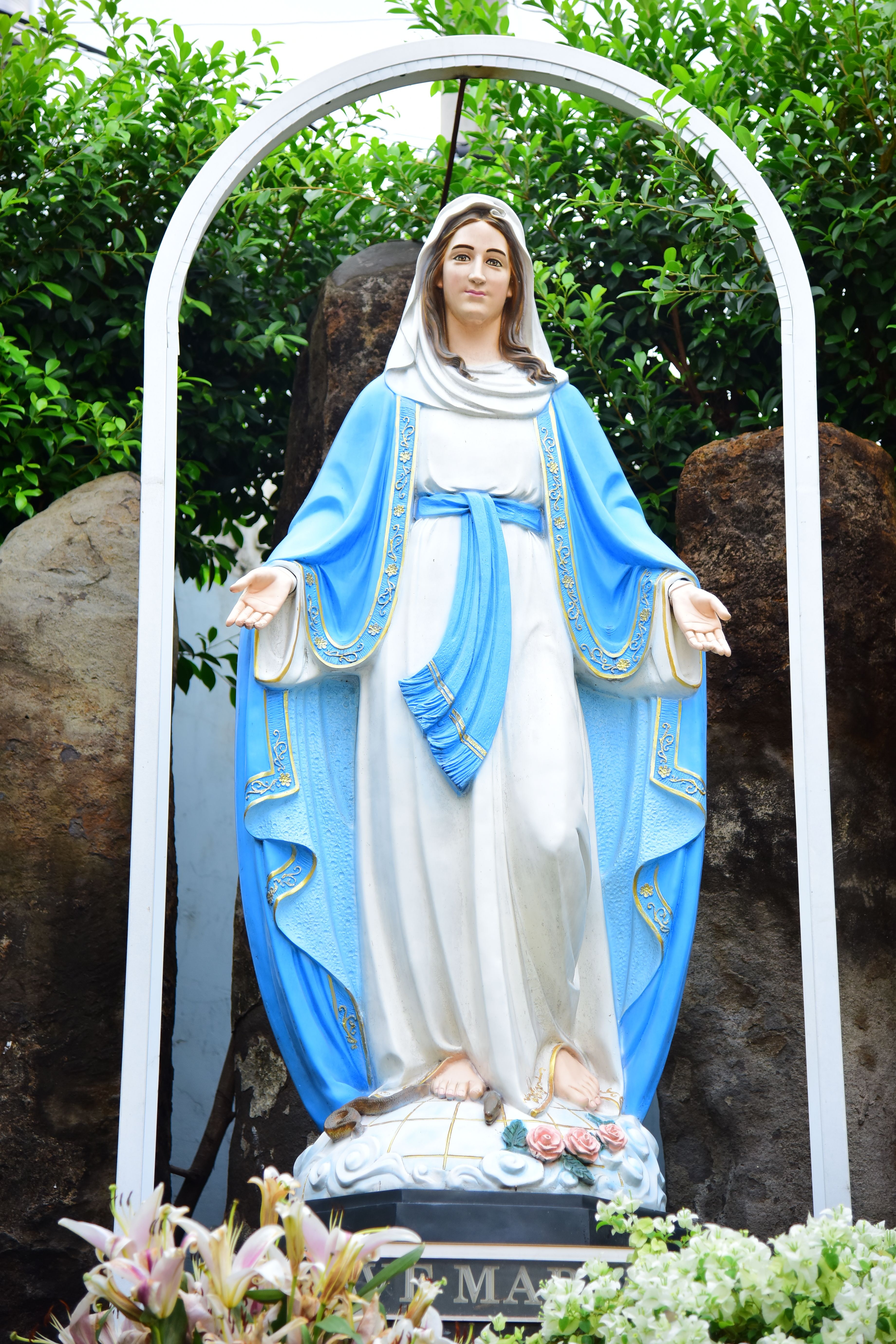 Statue of Virgin Mary with open arms in peaceful garden setting.