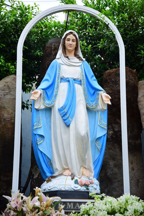 Free A serene statue of Virgin Mary with floral decor in an outdoor garden setting. Stock Photo