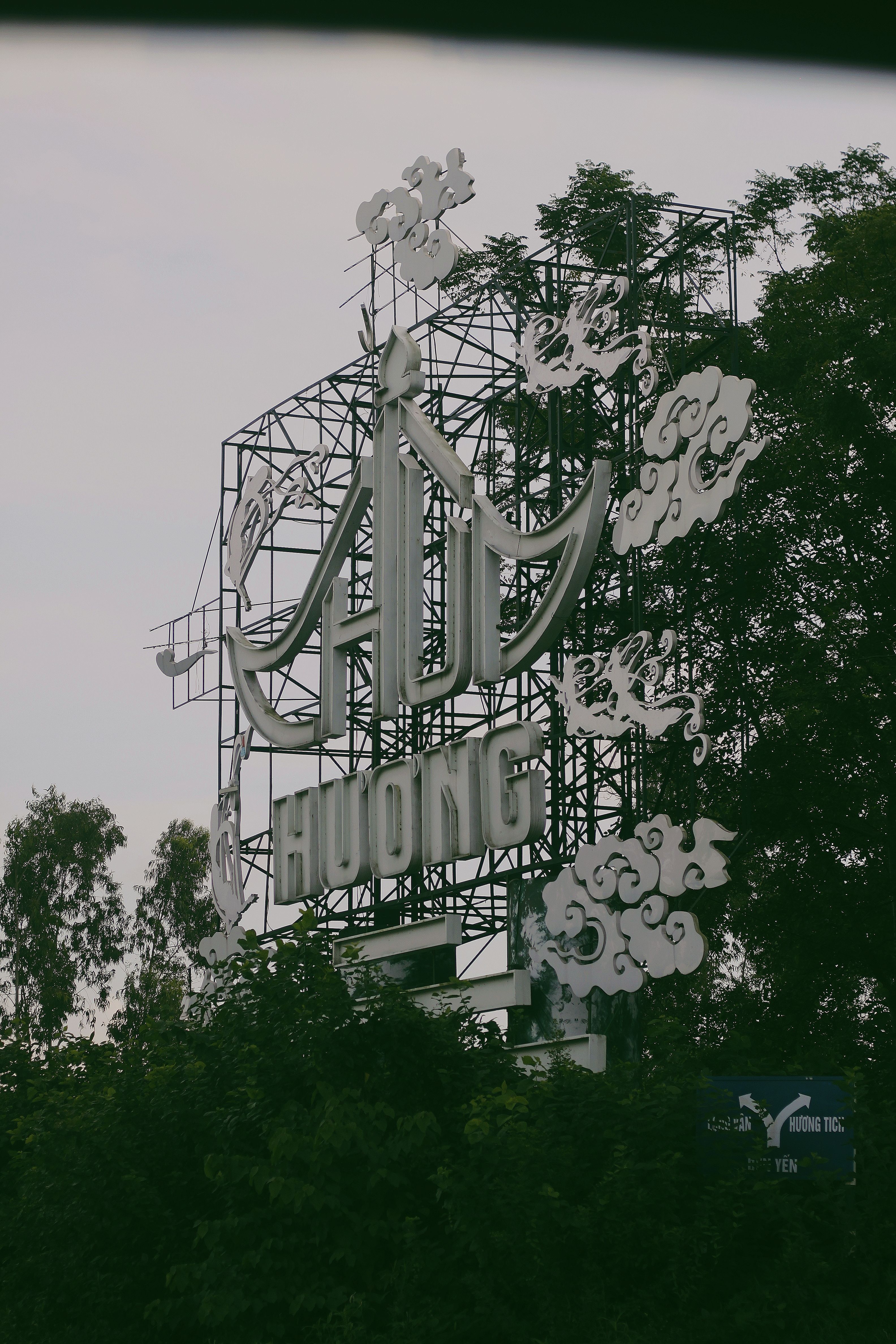 Outdoor metal signboard with artistic cloud motifs amidst trees.
