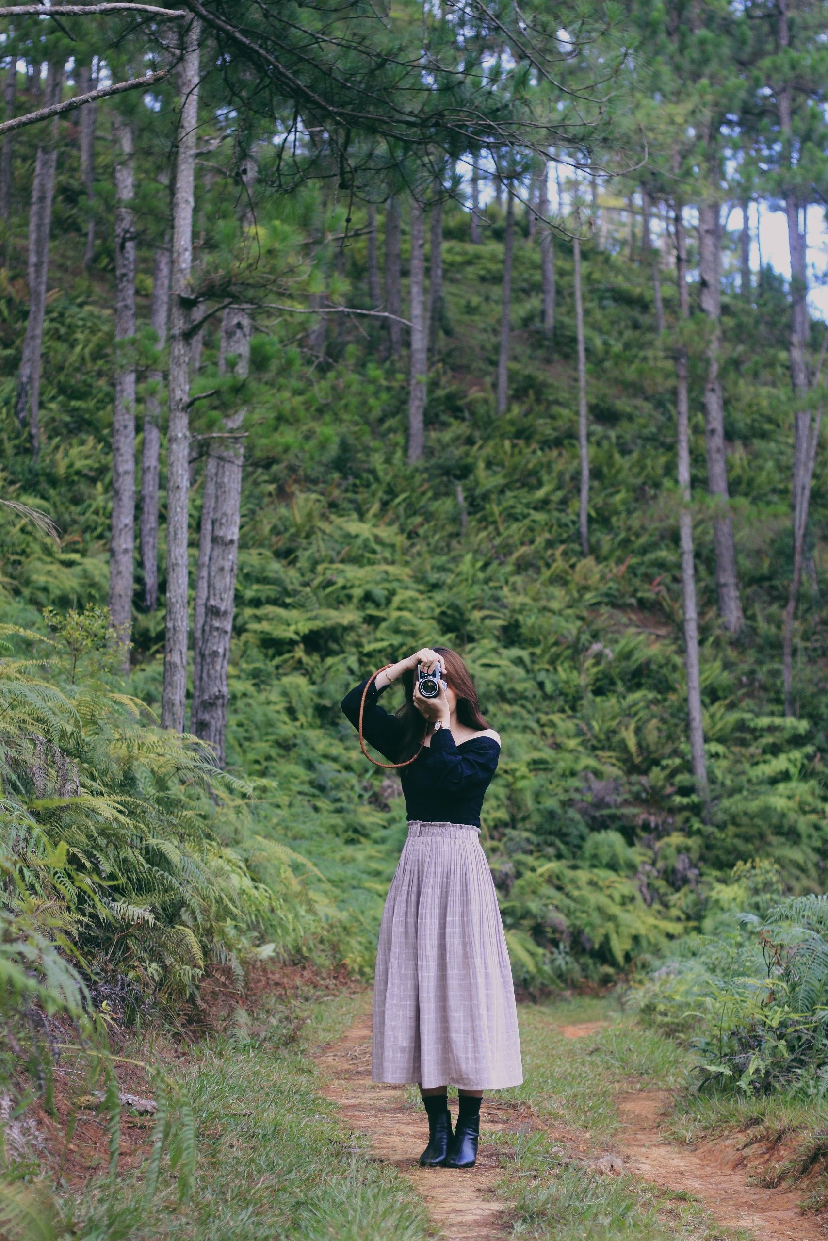 Woman photographing in a serene, lush forest capturing nature's beauty.