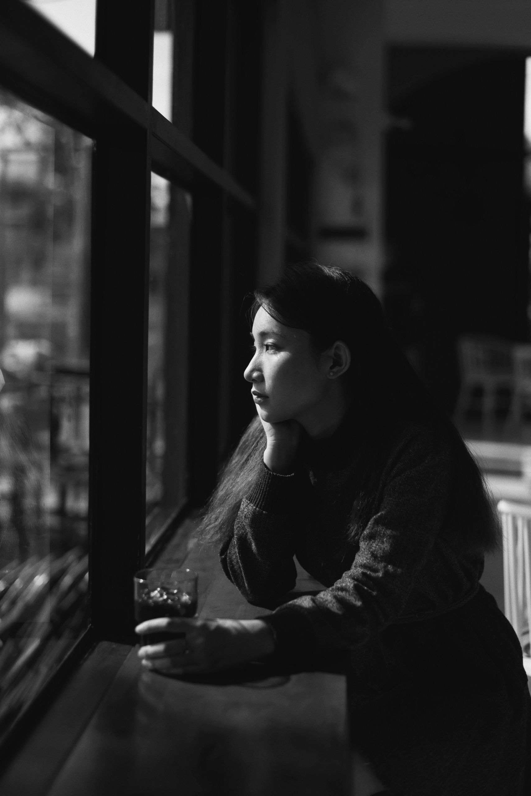 Black and white portrait of a woman thoughtfully looking outside a cafe window.
