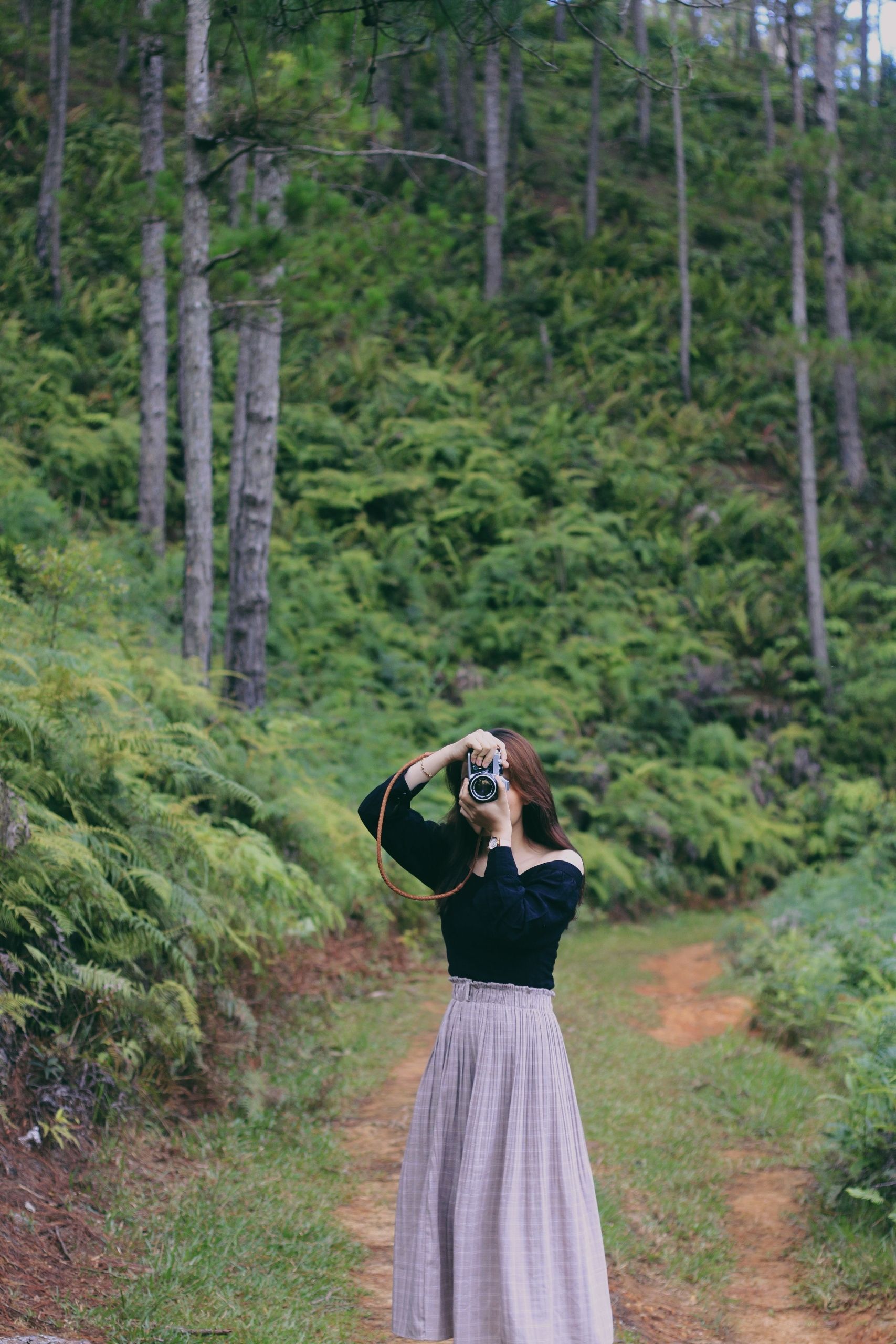A woman capturing nature with a camera on a serene forest pathway, embodying tranquility.