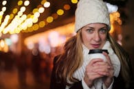 一位身着冬装的年轻女子在城市环境中享受着热饮，灯光被串起