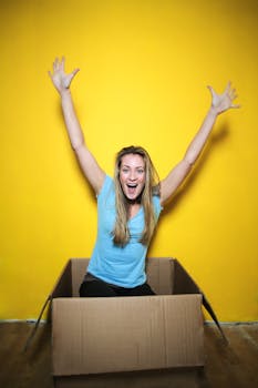 一位年轻女子在黄色背景的纸板箱里庆祝，她的头发很自然