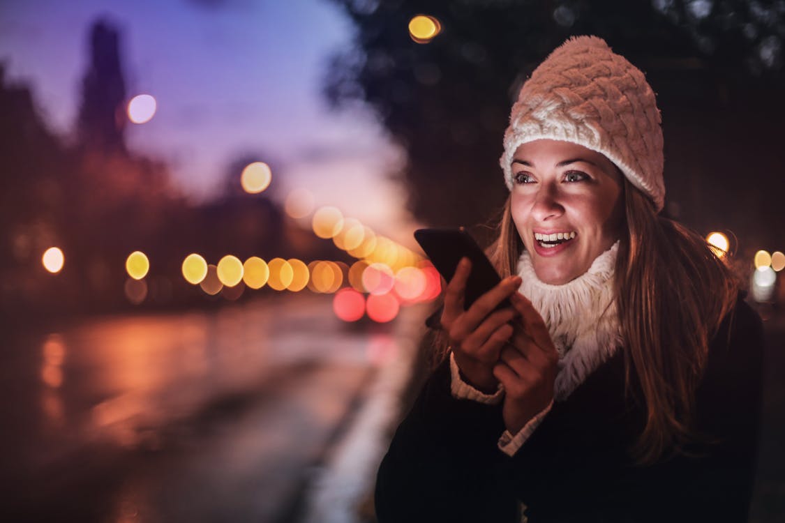 Cheerful woman recording voice message on smartphone in street