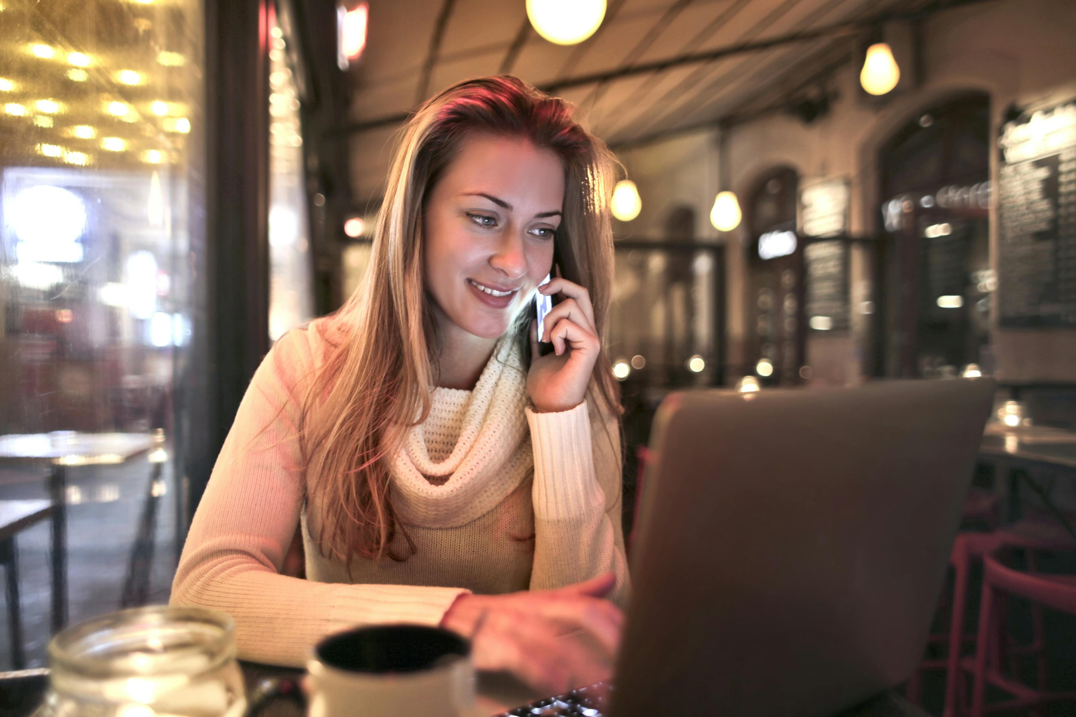 relaxed woman in cafe talking on smartphone and using laptop