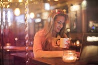 在柔和的烛光环绕下，一位女士在舒适的咖啡馆里轻松地享用着热咖啡