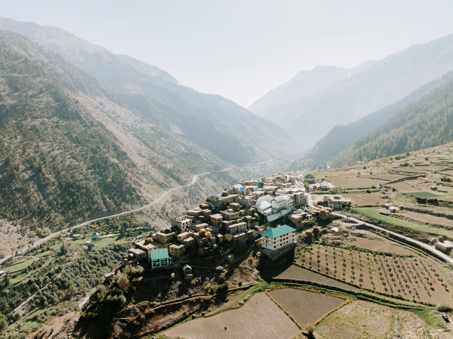A breathtaking aerial view of a scenic village nestled in the Himalayan mountains, surrounded by lush greenery.