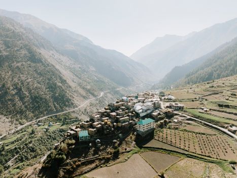 A breathtaking aerial view of a scenic village nestled in the Himalayan mountains, surrounded by lush greenery.