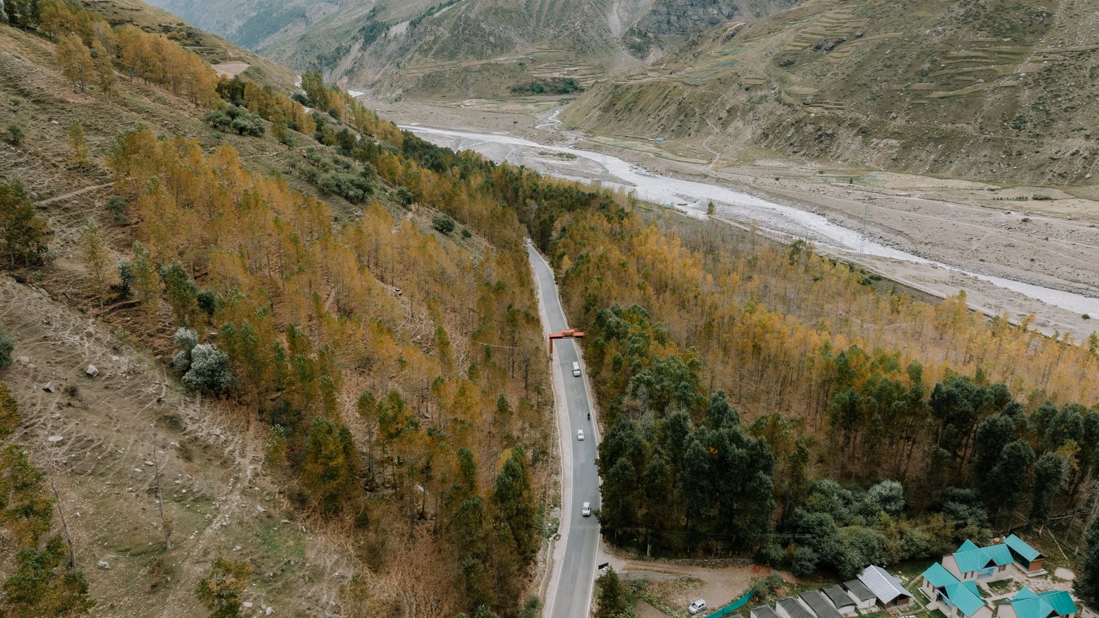 Aerial view of a winding road through a lush Himalayan valley with autumn foliage.