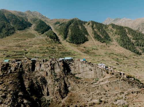 Free A picturesque Himalayan village nestled on a cliff with terraced fields and forested mountains behind. Stock Photo