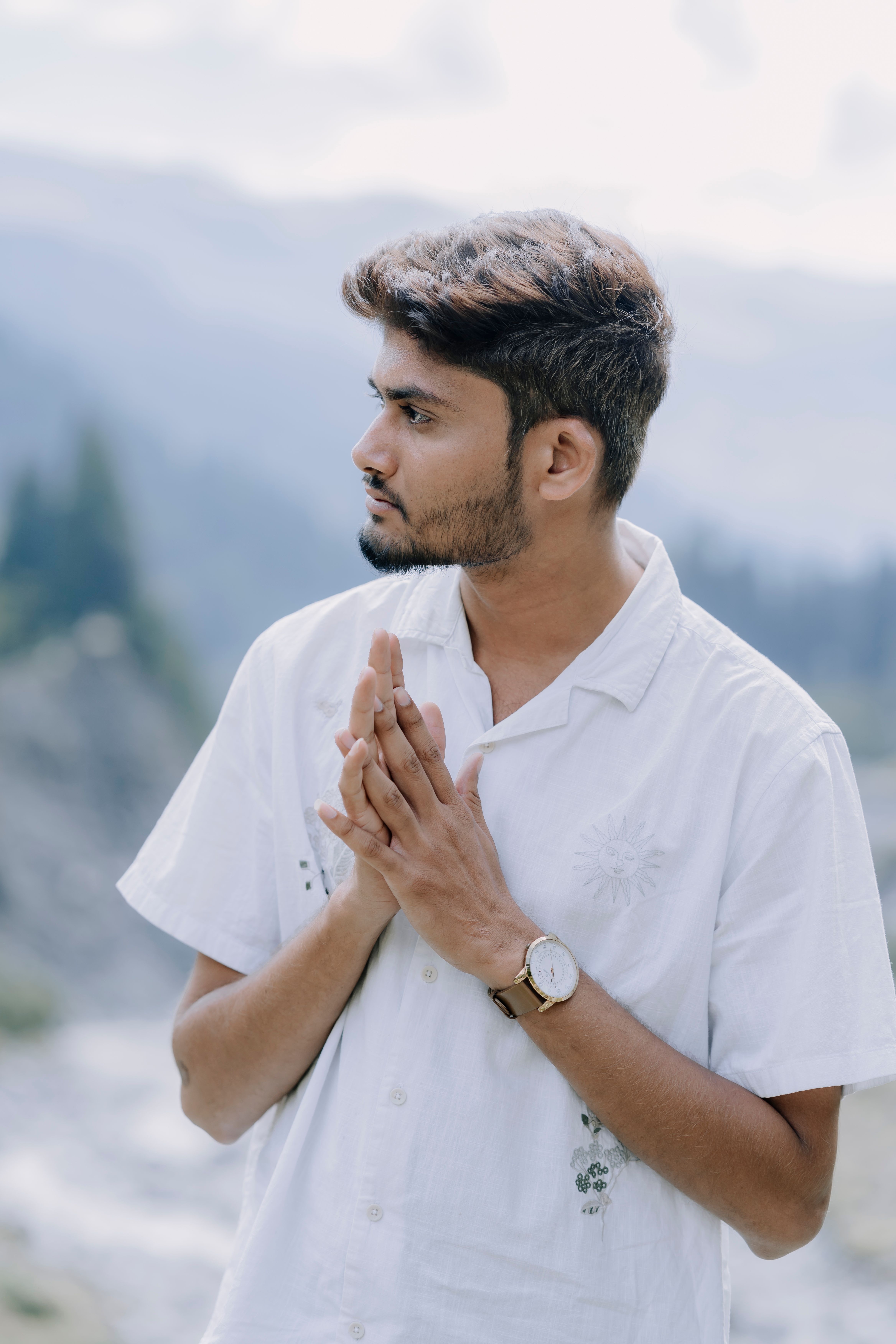 Young man in white shirt stands thoughtfully against a mountainous backdrop, capturing serenity and contemplation.