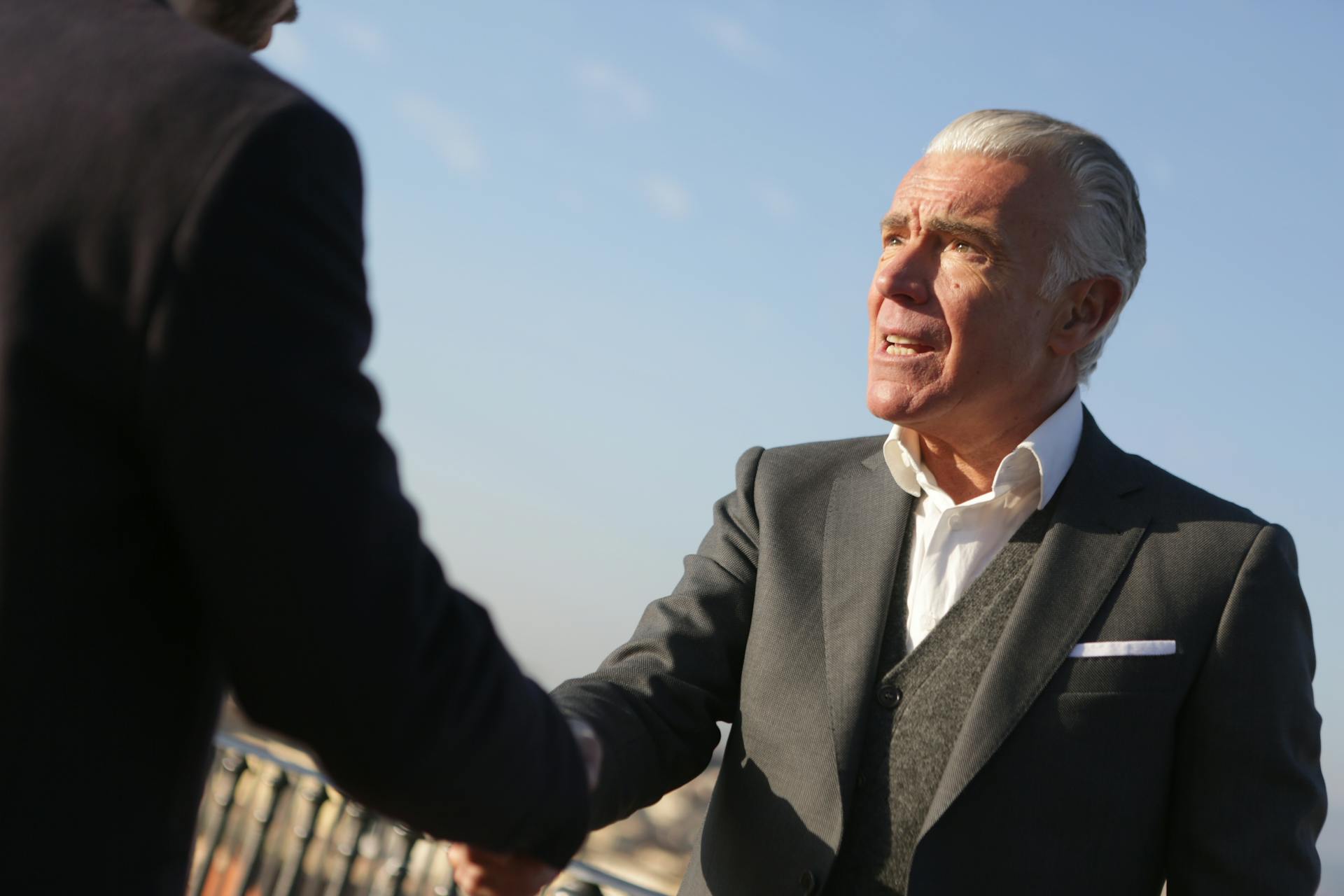 Elderly businessman shakes hands outdoors, symbolizing trust and cooperation.